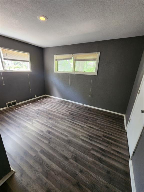 unfurnished room featuring a textured ceiling, visible vents, and dark wood-type flooring