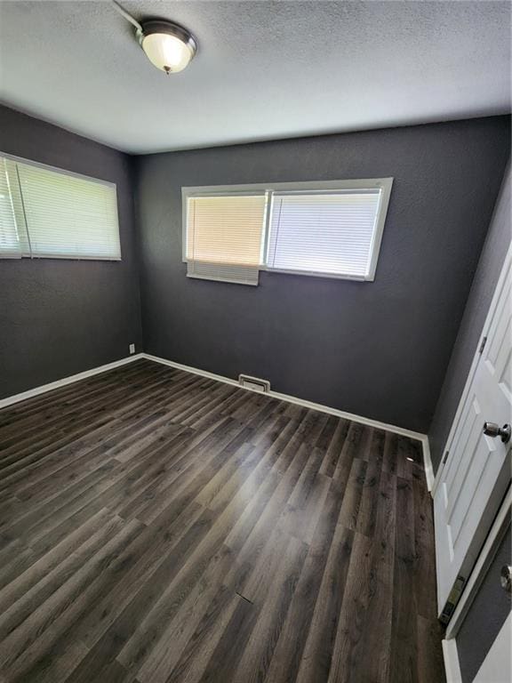 unfurnished bedroom with dark wood-type flooring, visible vents, a textured ceiling, and baseboards