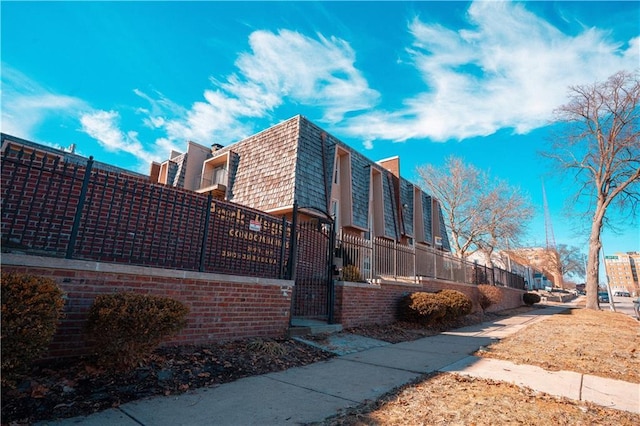 view of side of property featuring a fenced front yard, brick siding, and mansard roof