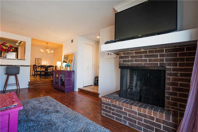 living area featuring visible vents, wood finished floors, a textured ceiling, a fireplace, and a chandelier