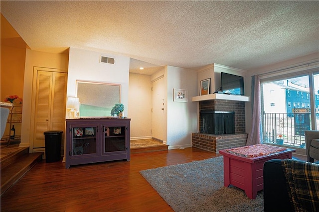 living room with a brick fireplace, a textured ceiling, visible vents, and wood finished floors