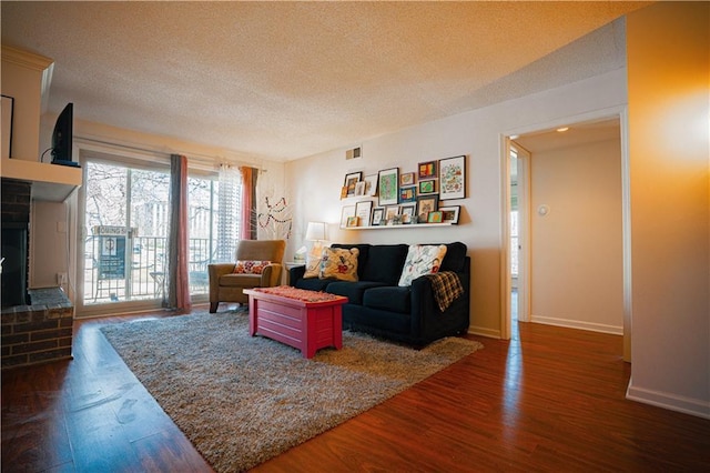 living area featuring a textured ceiling, a fireplace, visible vents, and wood finished floors