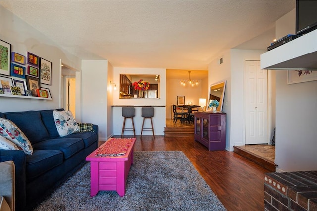 living room with visible vents, a textured ceiling, an inviting chandelier, and wood finished floors