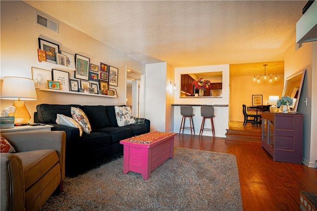 living room with a textured ceiling, wood finished floors, visible vents, and a chandelier