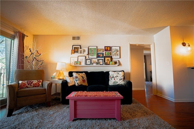 living room with baseboards, a textured ceiling, visible vents, and wood finished floors