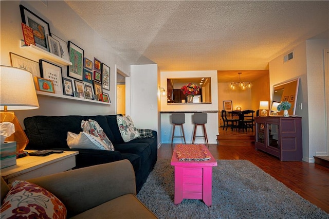 living room featuring a textured ceiling, wood finished floors, visible vents, and an inviting chandelier