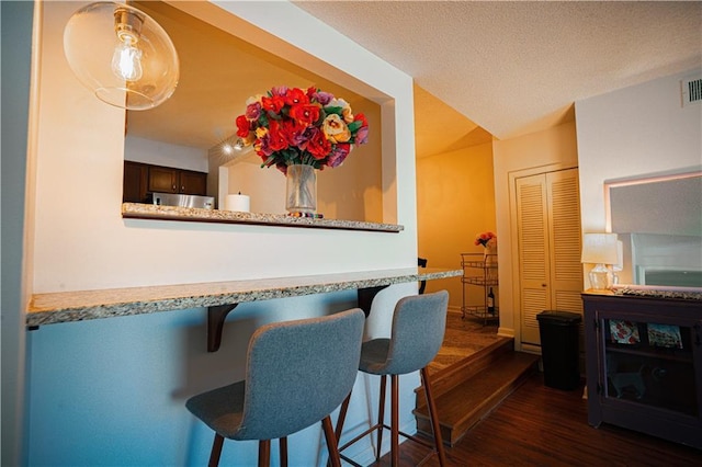 interior space with dark wood finished floors, a kitchen breakfast bar, a peninsula, a textured ceiling, and fridge