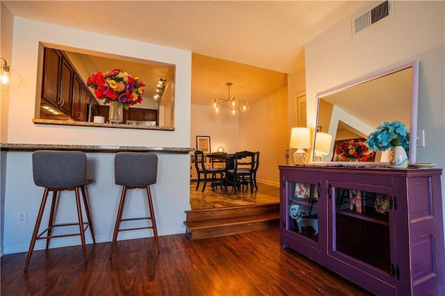 interior space with baseboards, visible vents, dark wood finished floors, an inviting chandelier, and a kitchen bar