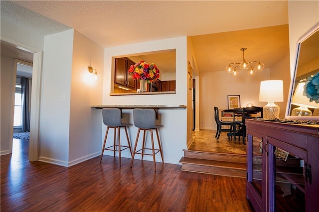 kitchen featuring dark wood-style floors, a kitchen bar, an inviting chandelier, a textured ceiling, and baseboards