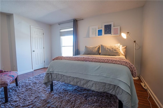 bedroom with a textured ceiling, wood finished floors, and baseboards