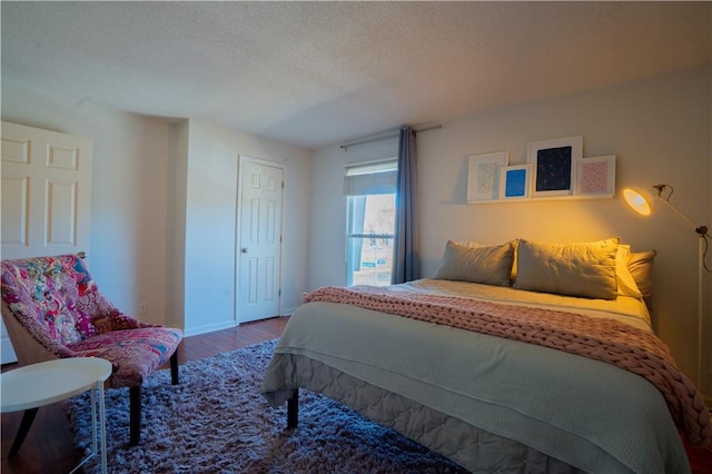 bedroom with a textured ceiling, baseboards, and wood finished floors