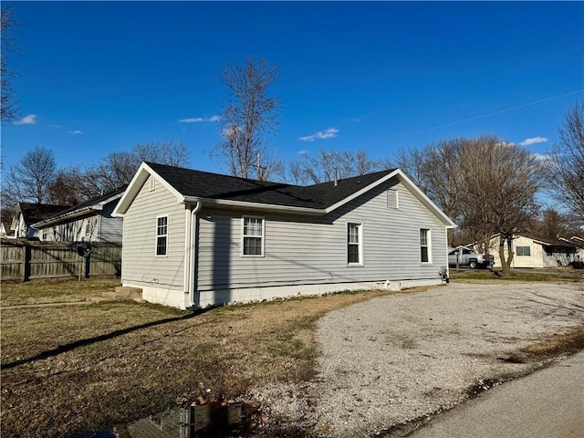 view of home's exterior featuring roof with shingles, driveway, and fence