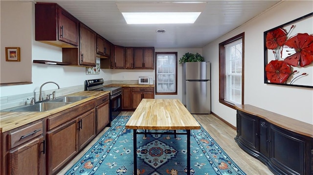 kitchen featuring appliances with stainless steel finishes, light wood-style floors, wooden counters, and a sink