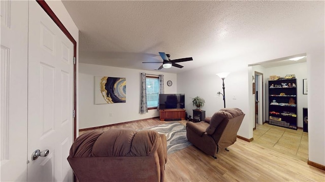 living room with baseboards, a ceiling fan, light wood-type flooring, and a textured ceiling