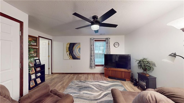 living room featuring visible vents, baseboards, wood finished floors, a textured ceiling, and a ceiling fan