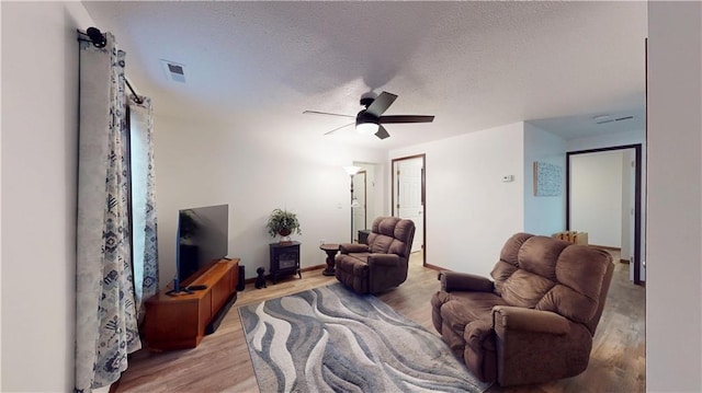 living room with a textured ceiling, wood finished floors, visible vents, and ceiling fan