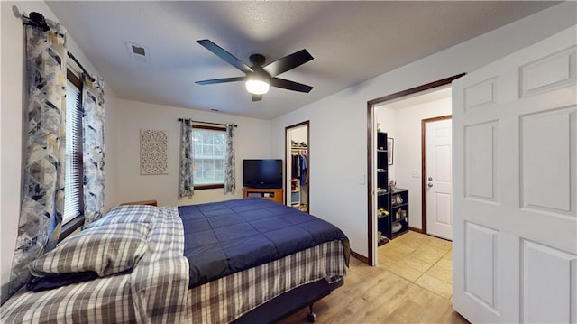 bedroom featuring a spacious closet, visible vents, ceiling fan, light wood-style floors, and a closet