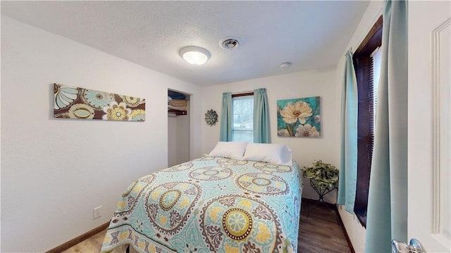 bedroom with baseboards, wood finished floors, visible vents, and a textured ceiling