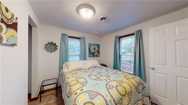 bedroom with visible vents, multiple windows, a textured ceiling, and wood finished floors