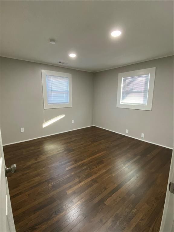 empty room featuring a healthy amount of sunlight, dark wood-type flooring, and recessed lighting