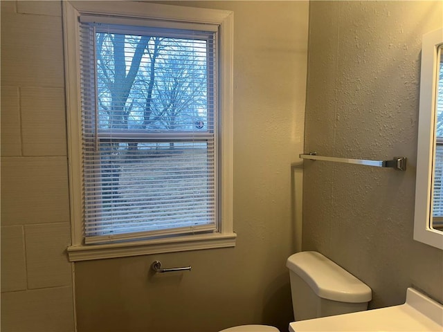 bathroom featuring a textured wall, plenty of natural light, vanity, and toilet