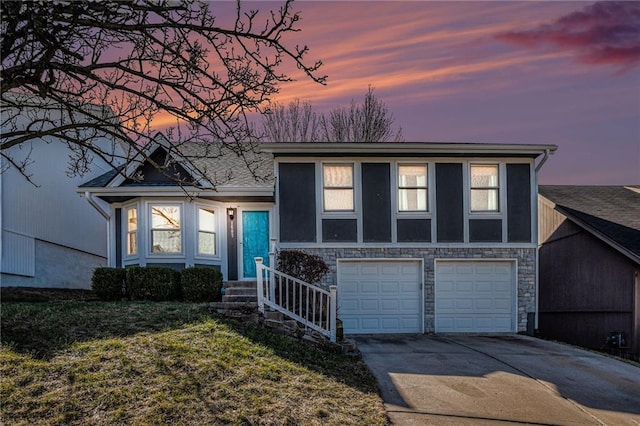 split level home with a yard, stone siding, driveway, and a garage