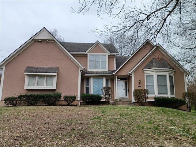 traditional-style house with roof with shingles, a front yard, and stucco siding