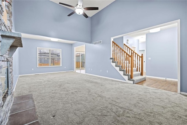 unfurnished living room with visible vents, carpet, stairs, a high ceiling, and a stone fireplace