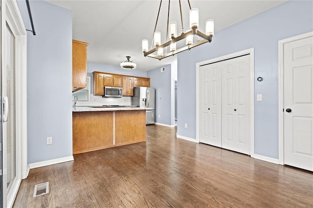 kitchen featuring visible vents, dark wood-style floors, a peninsula, stainless steel appliances, and a chandelier