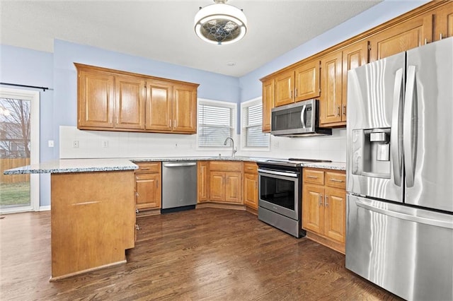 kitchen featuring stainless steel appliances, dark wood-style flooring, a sink, backsplash, and brown cabinets