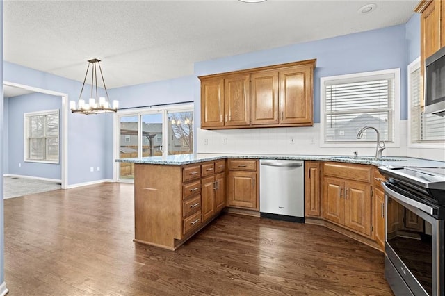 kitchen featuring dark wood-style floors, appliances with stainless steel finishes, brown cabinetry, a sink, and a peninsula