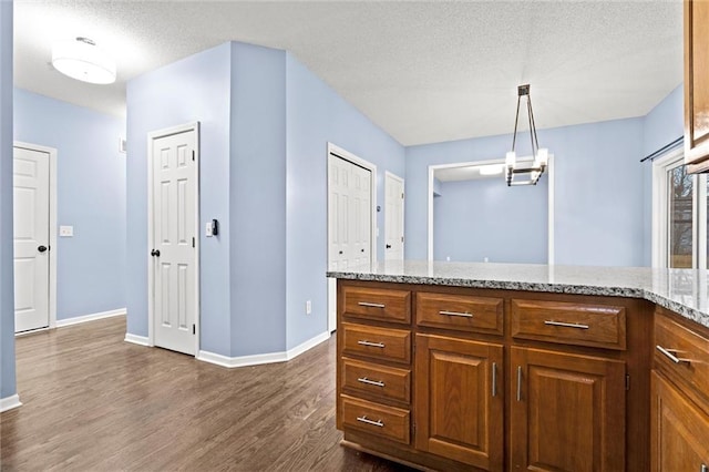 kitchen featuring dark wood-style floors, light stone counters, brown cabinetry, a textured ceiling, and baseboards