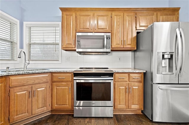 kitchen with tasteful backsplash, dark wood-style floors, appliances with stainless steel finishes, light stone countertops, and a sink