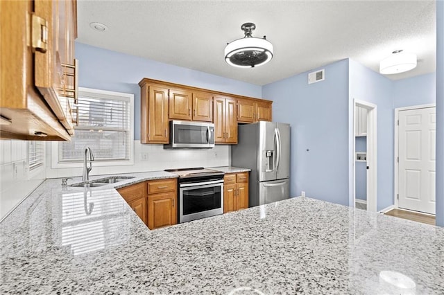 kitchen featuring visible vents, decorative backsplash, appliances with stainless steel finishes, light stone countertops, and a sink