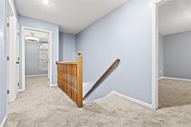 corridor featuring carpet floors, baseboards, a textured ceiling, and an upstairs landing