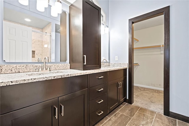 bathroom with a sink, baseboards, a tile shower, double vanity, and a walk in closet