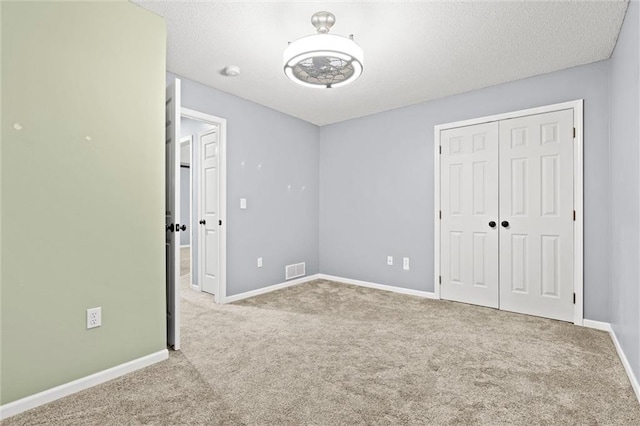 unfurnished bedroom with a closet, visible vents, carpet flooring, a textured ceiling, and baseboards