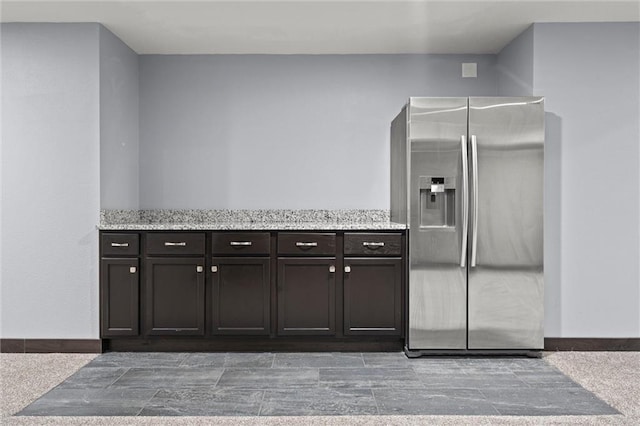 kitchen featuring dark brown cabinetry, light stone countertops, and stainless steel fridge with ice dispenser