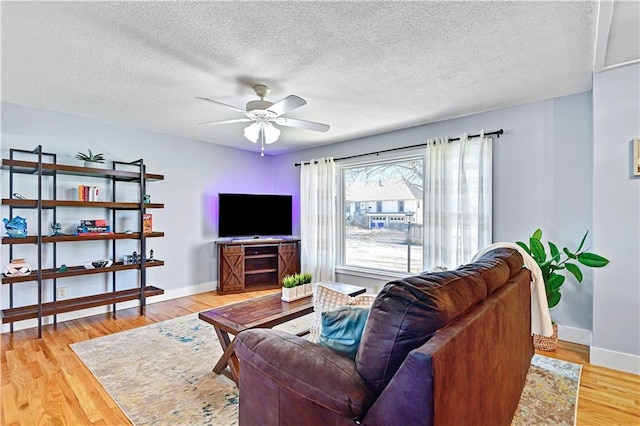 living room with a ceiling fan, wood finished floors, baseboards, and a textured ceiling