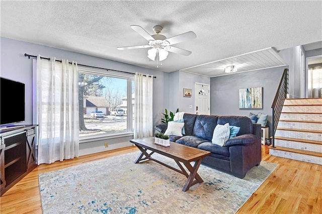 living room featuring stairway, a textured ceiling, ceiling fan, and light wood finished floors