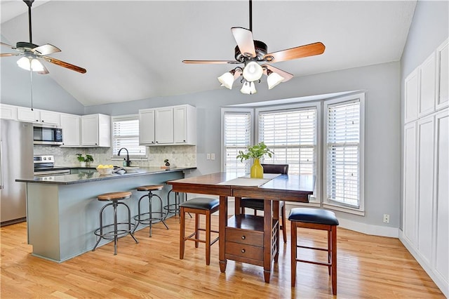 kitchen featuring tasteful backsplash, appliances with stainless steel finishes, a breakfast bar area, and light wood finished floors