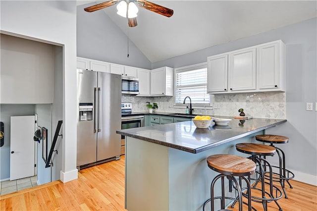 kitchen with a peninsula, light wood-style flooring, stainless steel appliances, white cabinets, and a kitchen breakfast bar