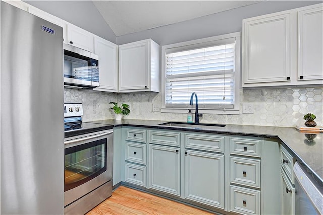 kitchen with a sink, backsplash, appliances with stainless steel finishes, and vaulted ceiling