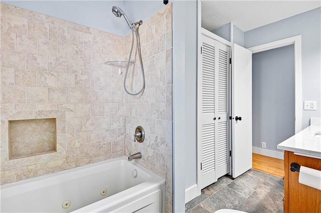 bathroom featuring a closet, vanity, a combined bath / shower with jetted tub, and baseboards