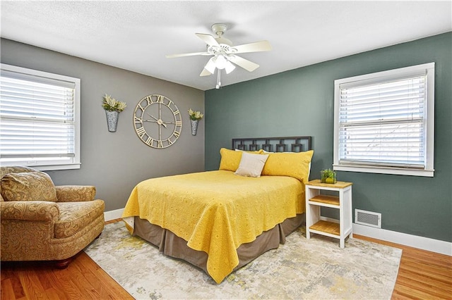 bedroom featuring a ceiling fan, wood finished floors, visible vents, and baseboards