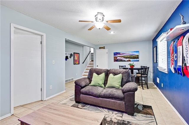 tiled living room with visible vents, baseboards, ceiling fan, stairway, and a textured ceiling