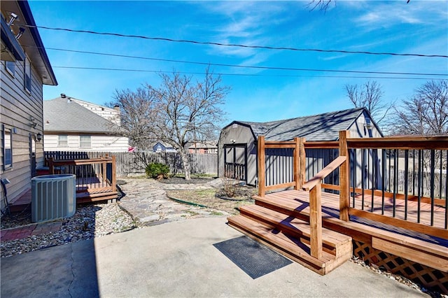 view of patio / terrace featuring cooling unit, a wooden deck, a fenced backyard, an outdoor structure, and a storage shed