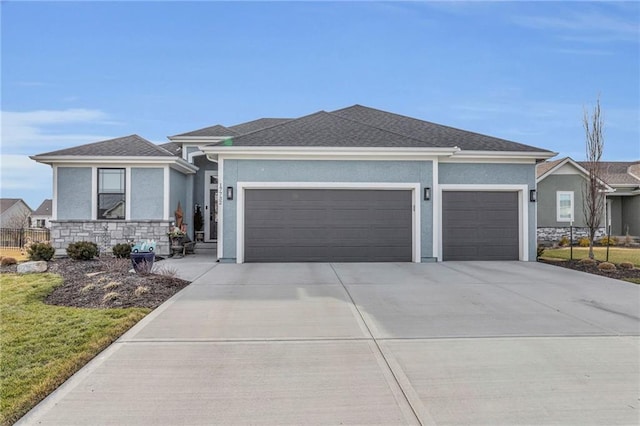 view of front facade featuring driveway, a shingled roof, stone siding, an attached garage, and stucco siding