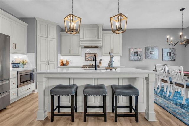 kitchen featuring a center island with sink, stainless steel appliances, light countertops, light wood-style floors, and a chandelier