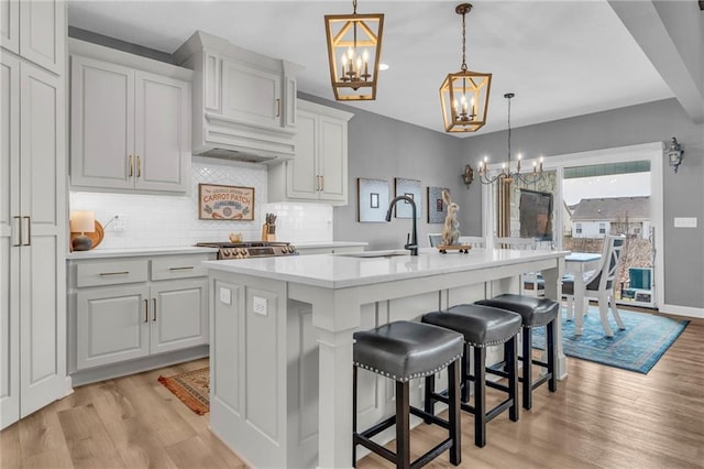 kitchen featuring light countertops, a sink, an island with sink, and an inviting chandelier